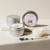 Three metal tins with 'Point Blank' labels, a lit candle, and a lavender sprig on a light surface.