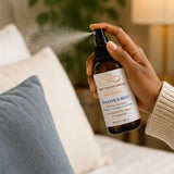 Hand using Breathe & Reset Room & Linen Spray to refresh a room with a botanical mist.