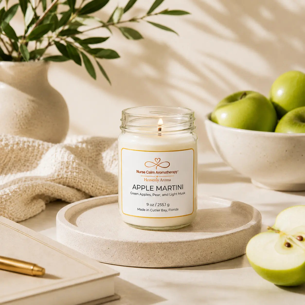 Candle labeled 'Apple Martini' on a decorative plate with apples and a plant in the background.