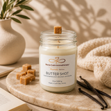 Jar of 'Butter Shot' candle from Nurse Calm Aromatherapy on a marble surface with vanilla beans and a plant in the background.