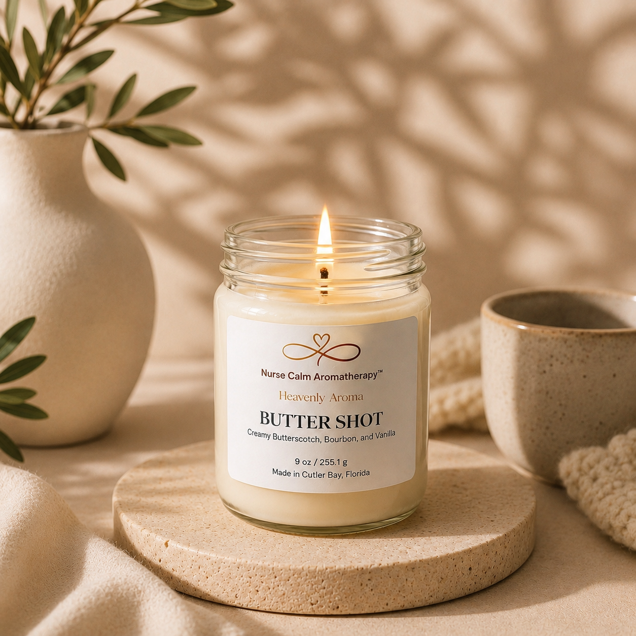Candle in a glass jar labeled 'Butter Shot' by Nurse Calm Aromatherapy on a wooden stand with a neutral background.