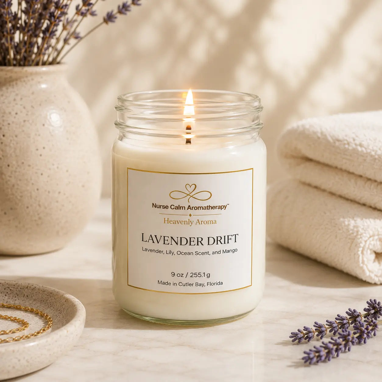 Candle labeled 'Nurse Calm Aromatherapy Nurse Calm Aromatherapy™ by Heavenly Aroma Lavender Drift' with lavender flowers and a towel in the background.
