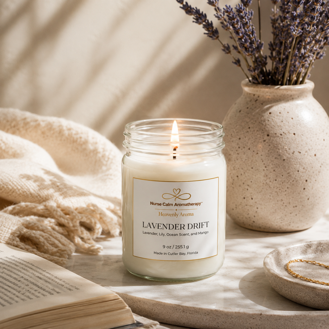 Candle in a glass jar labeled 'Nurse Calm Aromatherapy' with lavender in a vase on a neutral background