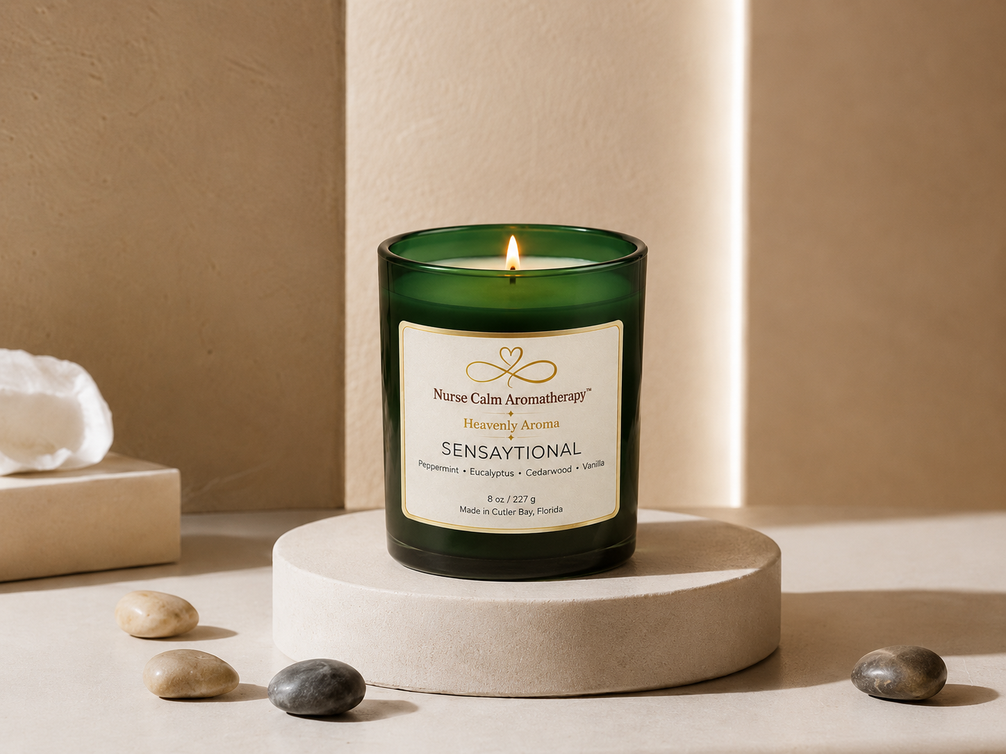 Sensaytional soy candle by Nurse Calm Aromatherapy™ displayed on a neutral cream pedestal with soft spa-inspired décor. Green glass candle with gold-trimmed label and lit flame featuring peppermint, eucalyptus, cedarwood, and vanilla fragrance notes.
