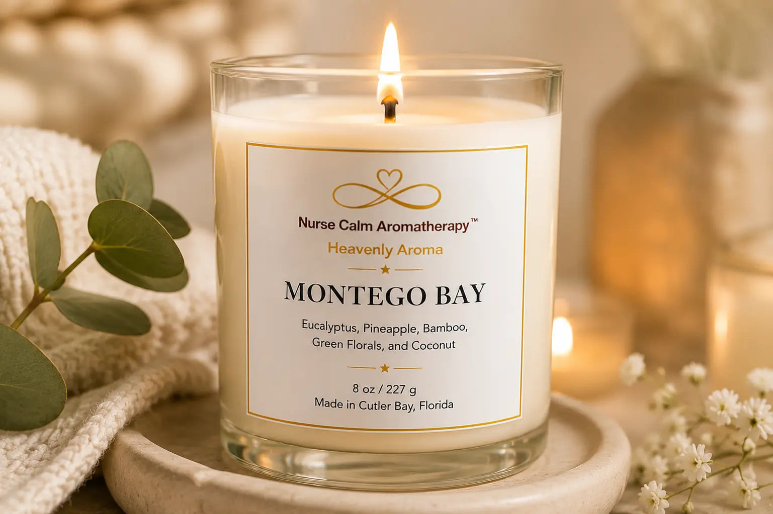 A lit candle in a clear glass jar with a white label reading 'Nurse Calm Aromatherapy' and 'Montego Bay,' styled on a wooden tray with soft warm lighting and eucalyptus leaves around it.